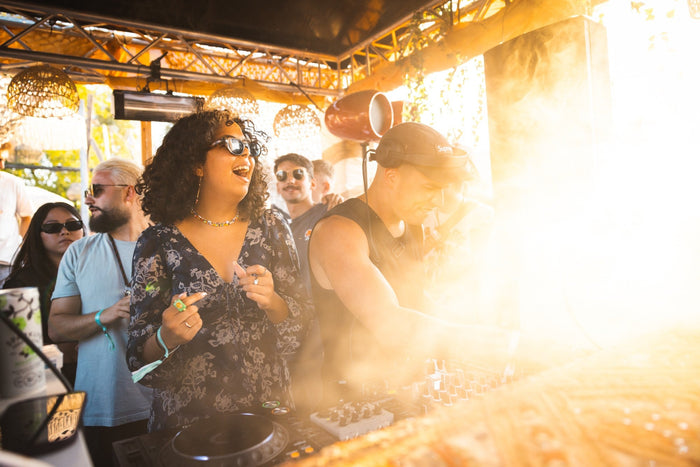 DJ playing at an open air booth while the sun flares into the frame