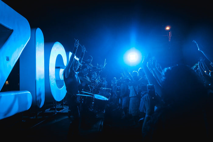 Drummers performing next to illuminated letters in blue light