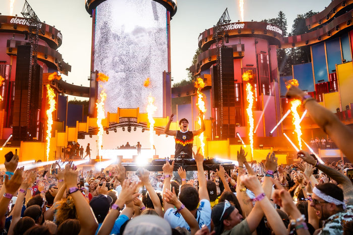 Artist on stage between flame jets with raised hands in the crowd