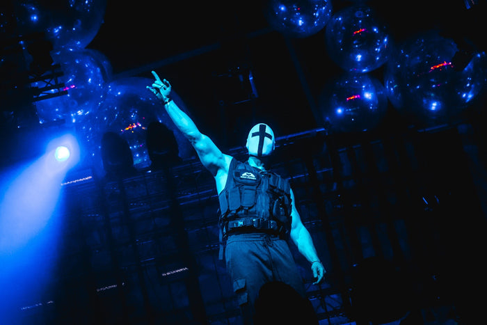 Masked performer pointing upwards under blue balloons
