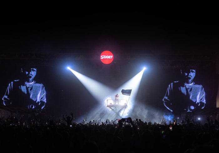 Artist alone on a lifted platform in two spotlights above the night crowd