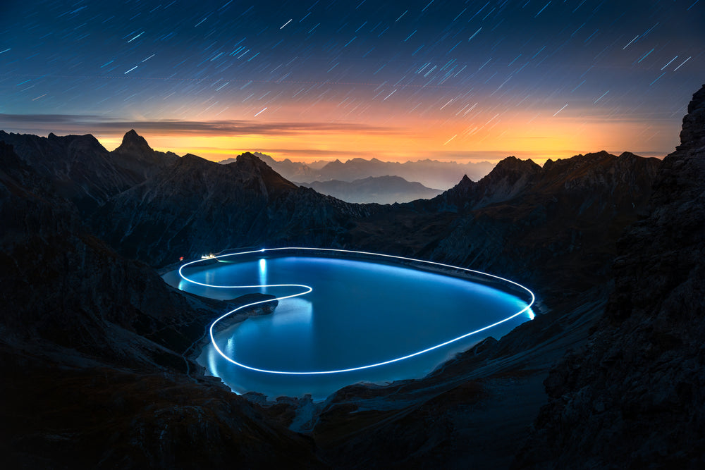 Glowing heart of light drawn with a drone around Luenersee at night, star trails over the Alps, Vorarlberg, Austria, by Lucas Tiefenthaler