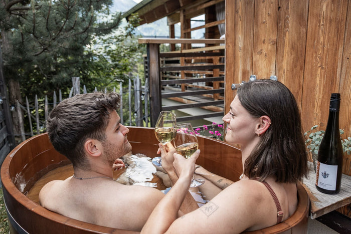 Couple toasting with white wine in a wooden hot tub at the chalet