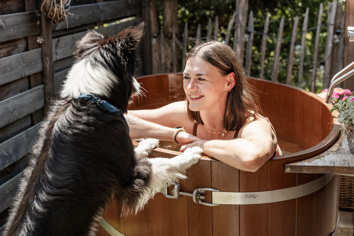 Border collie greeting a smiling guest in a wooden hot tub