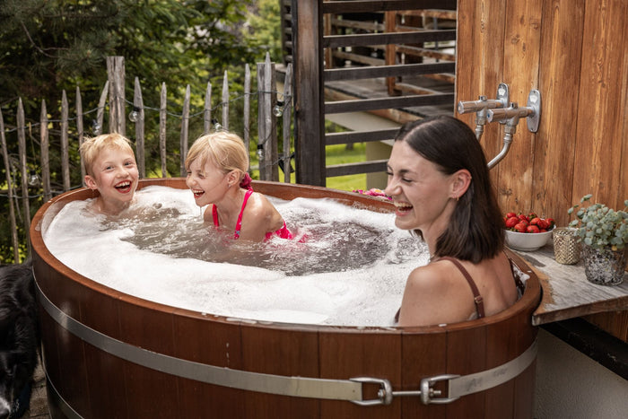 Two children and a woman laughing in a wooden hot tub