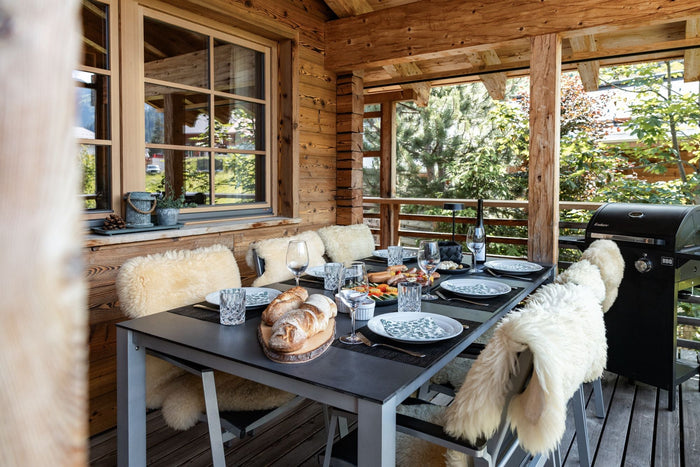 Covered chalet terrace with a set dinner table, sheepskins and a barbecue