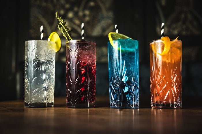 Four colourful long drinks in cut glasses on a bar counter