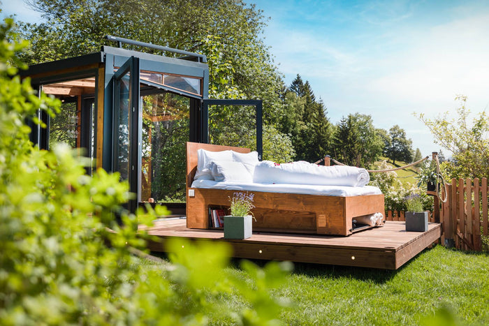 Outdoor bed in front of an open glass suite in the garden