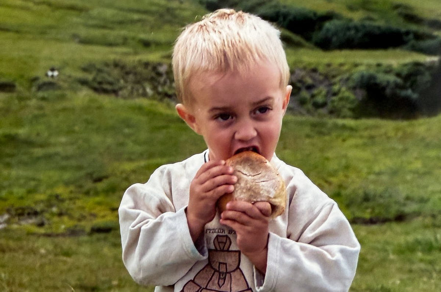Lucas as a kid eating a bread roll on an alpine meadow