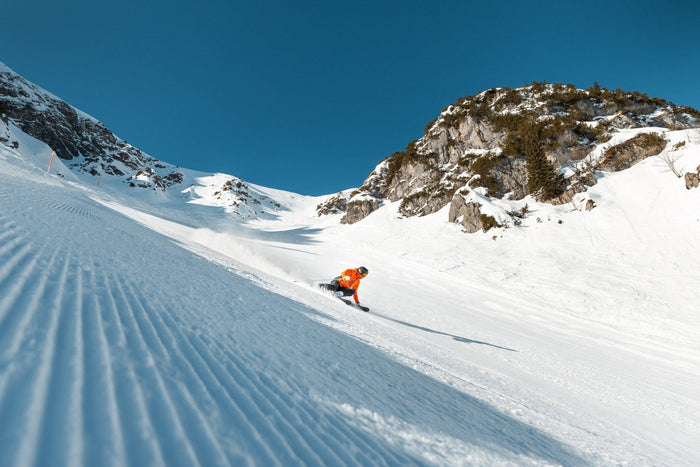 Skier in an orange jacket carving a freshly groomed piste