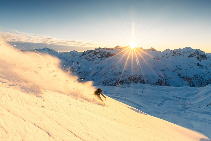 Skier descending a golden slope while the sun sets behind the peaks
