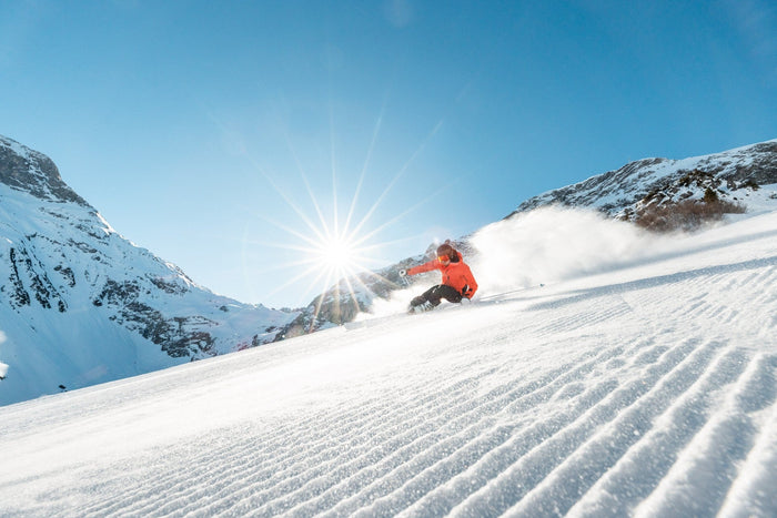 Skier carving corduroy with a sunburst between two peaks