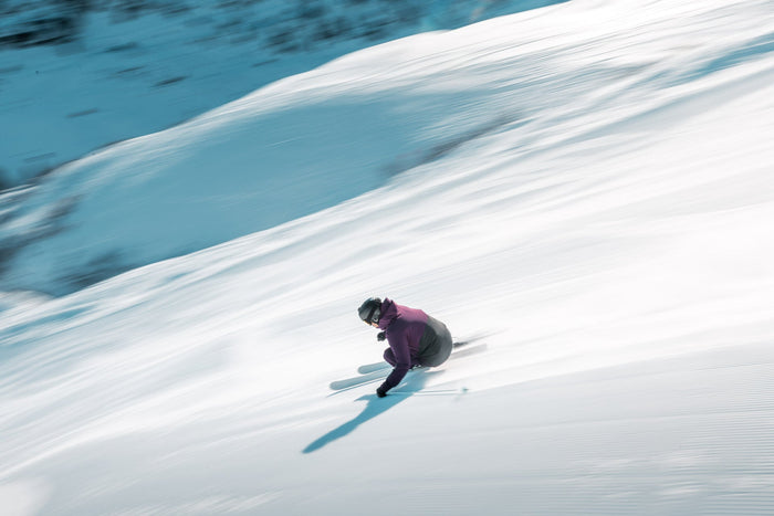 Panning shot of a skier in purple sweeping down a sunlit slope