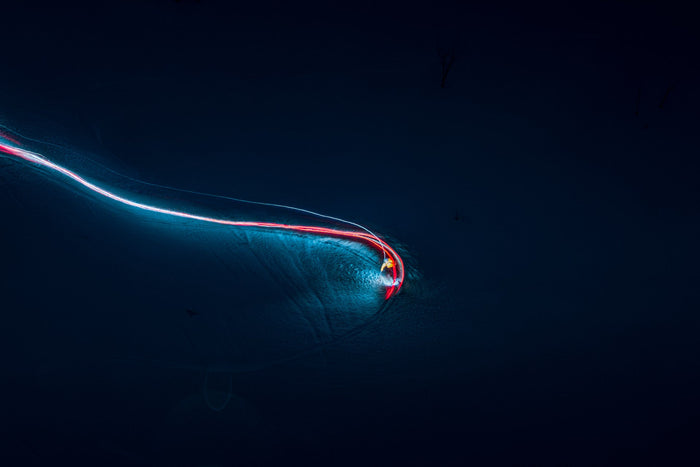 Light painting of a skier drawing a red and white line through the night