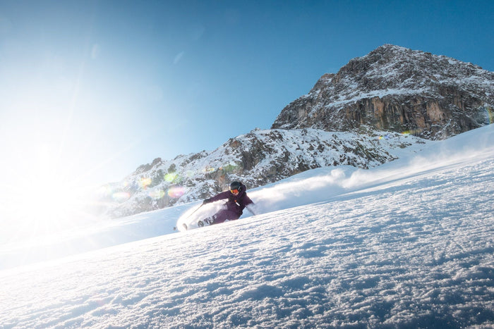 Skier in a purple suit throwing powder against the low sun