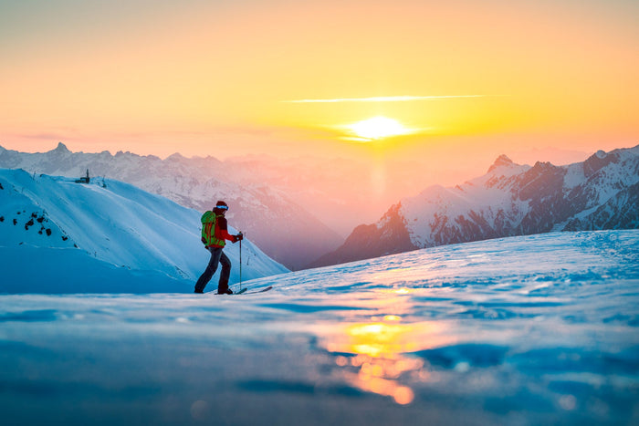 Ski tourer walking into a golden sunrise above a sea of peaks