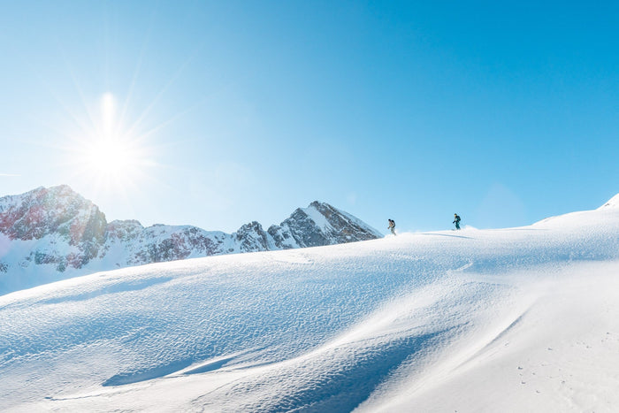 Two ski tourers walking a sunlit ridge above untouched snow fields