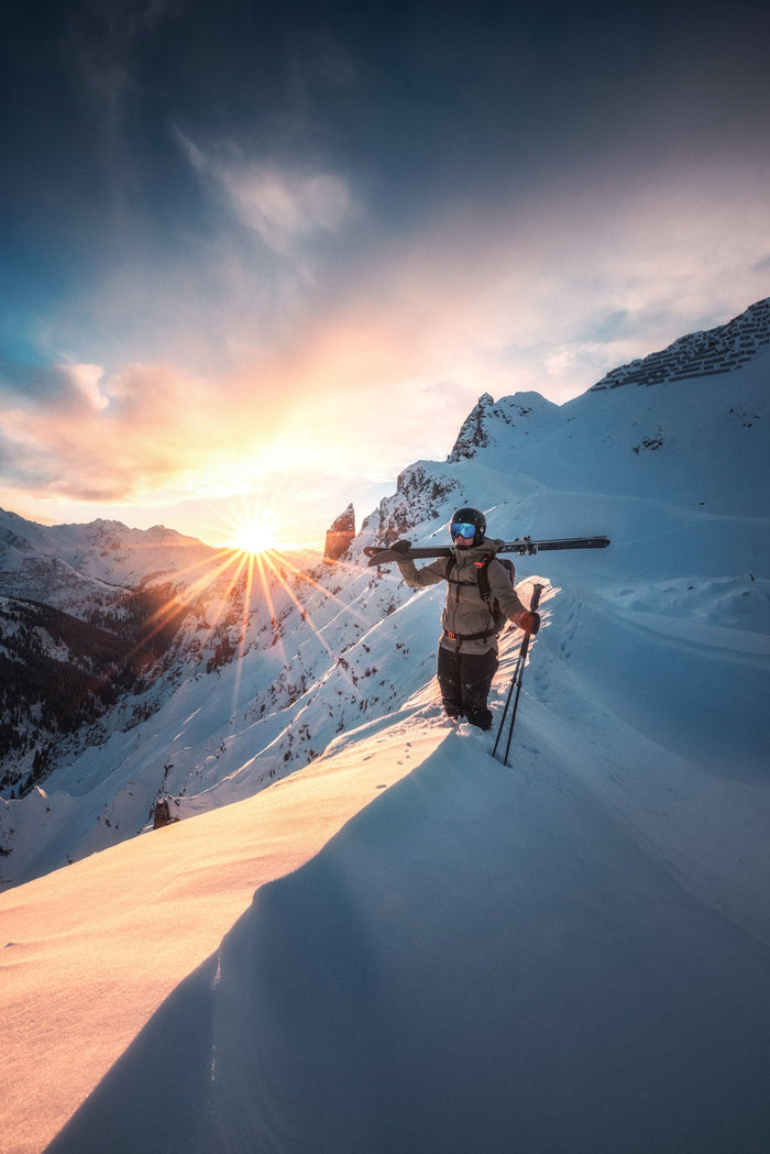 Skier carrying skis along a snowy ridge at sunrise at the Arlberg