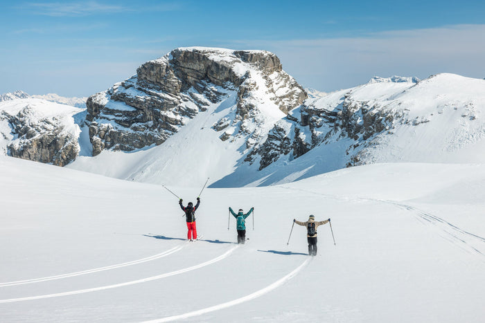 Three skiers raising their arms in front of a rocky peak