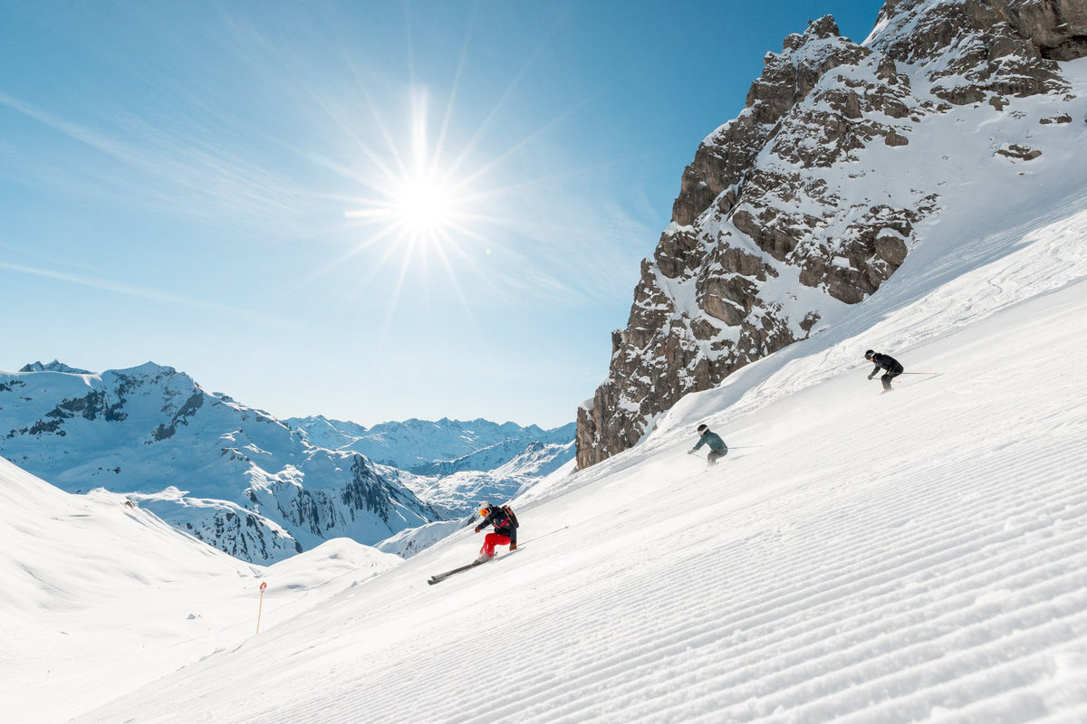 Three skiers carving down a groomed piste under a sunstar