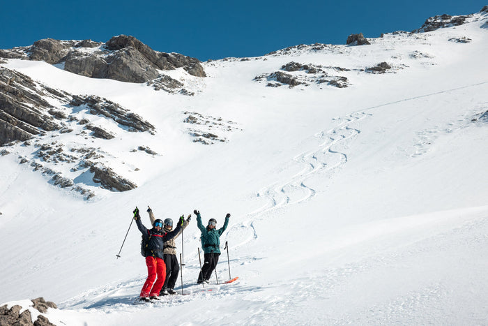 Three skiers celebrating below their fresh tracks in a steep slope