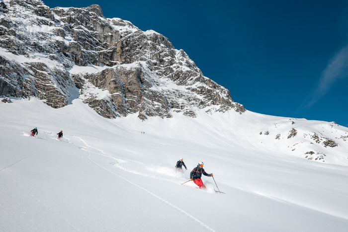 Three freeriders descending an open powder slope below a rock face in Zürs