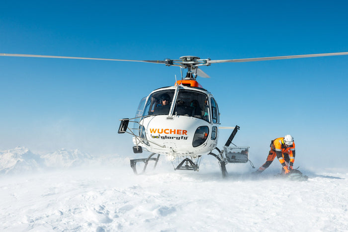 Helicopter landing in blowing snow while a guide crouches beside it