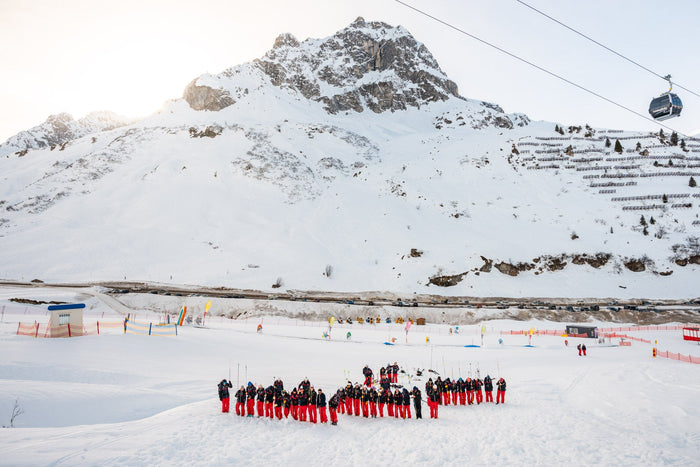 Skischule Zürs instructor team in red trousers forming a shape below the mountain