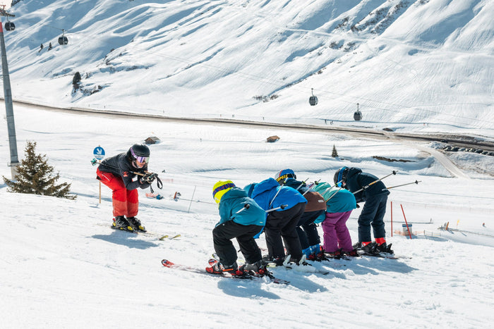 Children copying their ski instructor in a tuck position on the piste