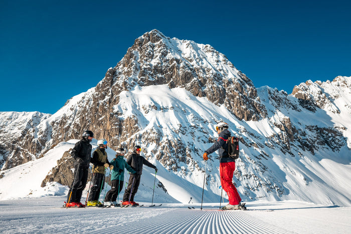 Ski instructor briefing a group on a groomed piste below a rocky peak