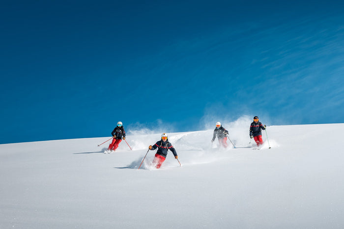 Four instructors skiing powder against a deep blue sky