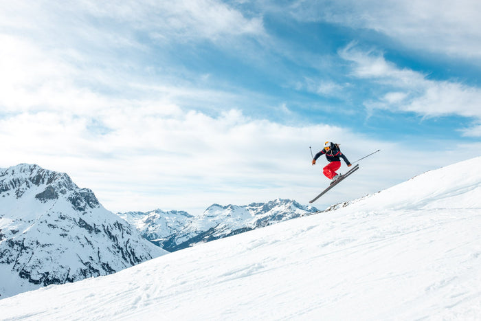 Skier jumping off a snowy ridge against clouds above Zürs