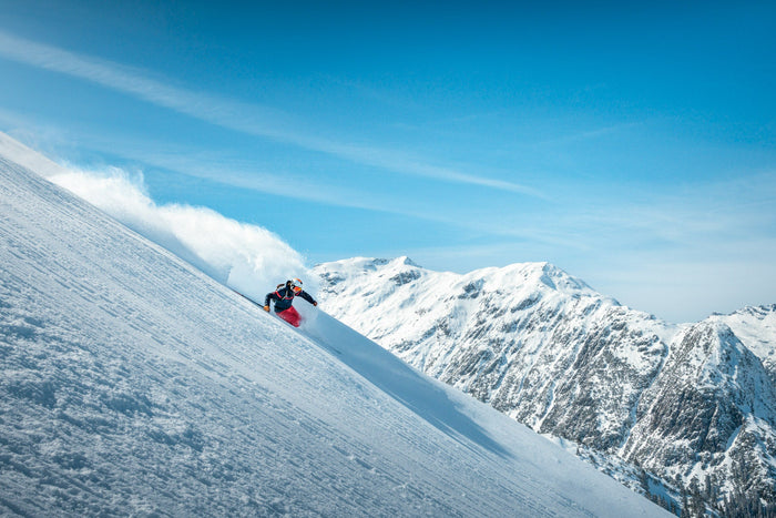 Skier throwing powder on a steep slope with Arlberg peaks behind