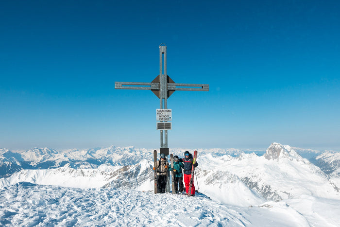 Group of ski tourers at a summit cross above a sea of peaks