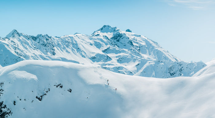 Drone panorama of three skiers on a snowy ridge below Arlberg peaks