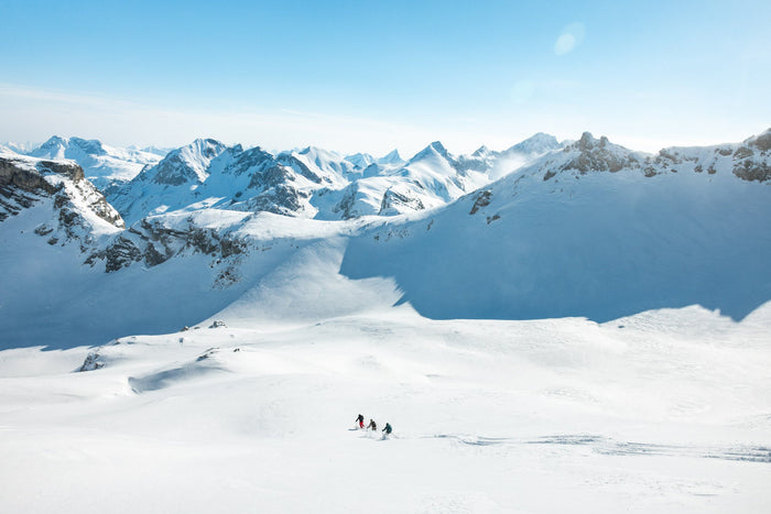 Three small skiers in a wide snowy bowl surrounded by Arlberg peaks