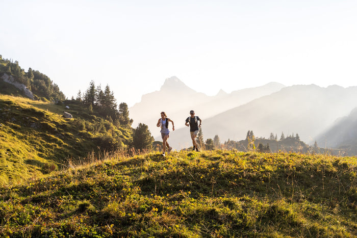 Two trail runners on a golden meadow with hazy peaks behind