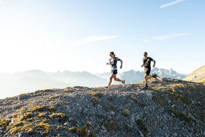 Two trail runners on a gravel ridge in morning light above Lech Zürs
