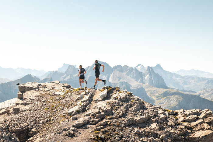 Two trail runners on a ridge with jagged Arlberg peaks behind