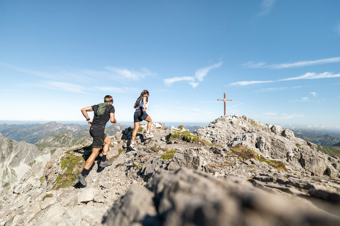 Two trail runners heading for a summit cross on a limestone ridge