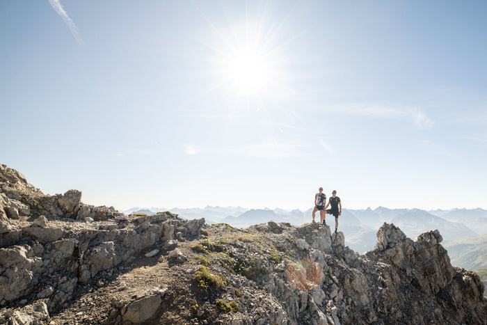 Two trail runners standing on a rocky summit under a sunstar