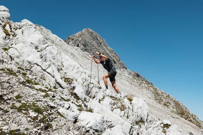 Trail runner pushing uphill with poles below a rocky peak