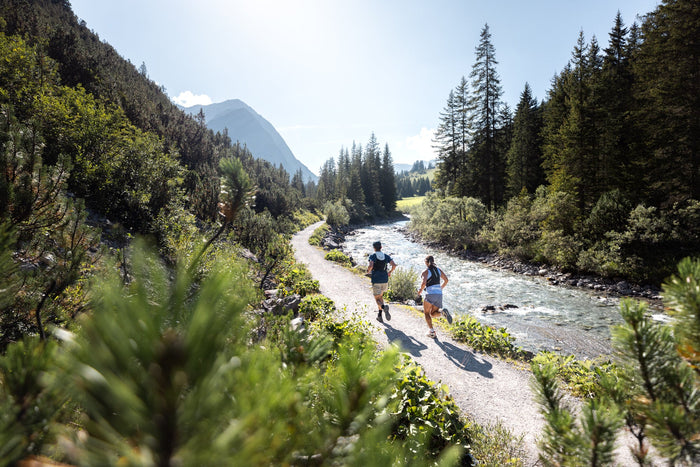 Two trail runners on a gravel path beside a mountain river