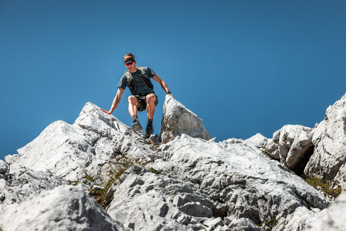 Trail runner climbing down between limestone blocks under a deep blue sky