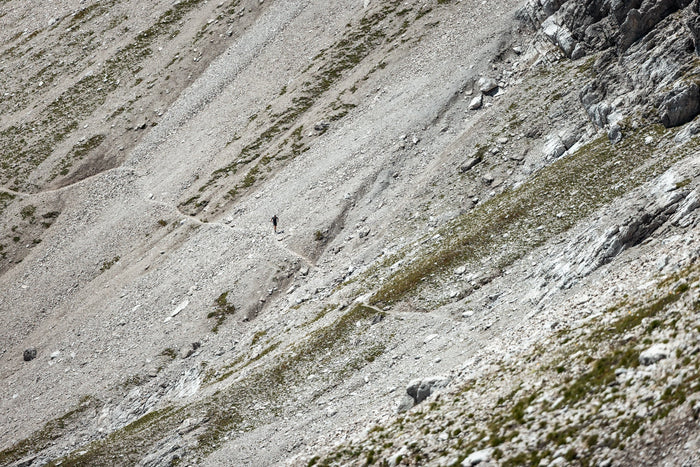 Tiny trail runner on a path across a huge scree slope