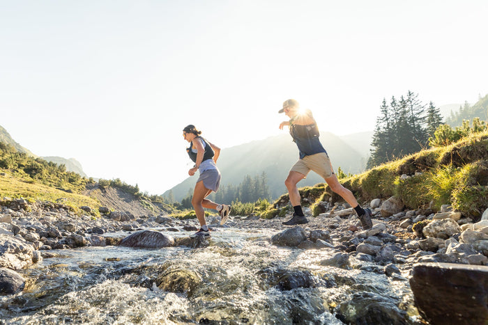 Two trail runners crossing a stream in backlight