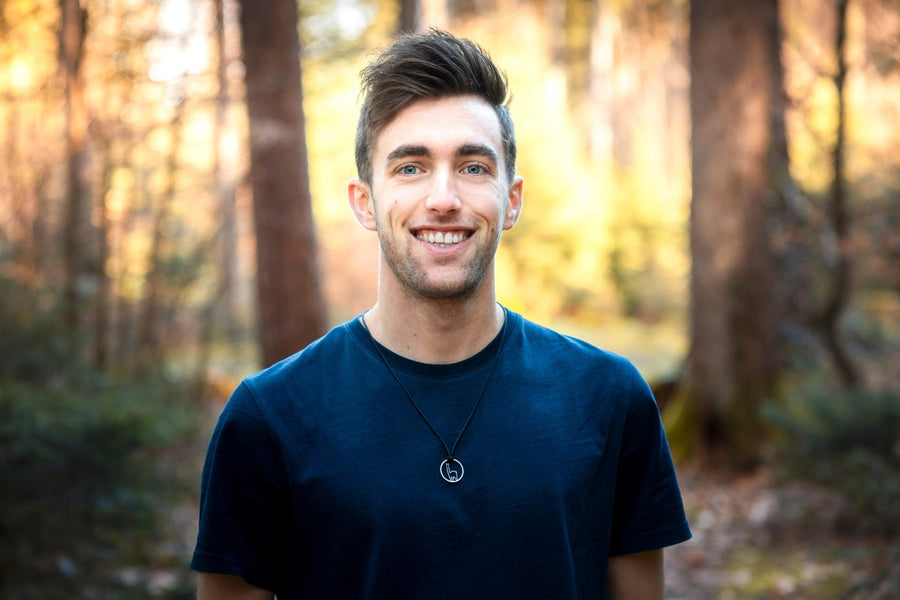 Portrait of Lucas Tiefenthaler smiling in the forest, wearing his mountain necklace
